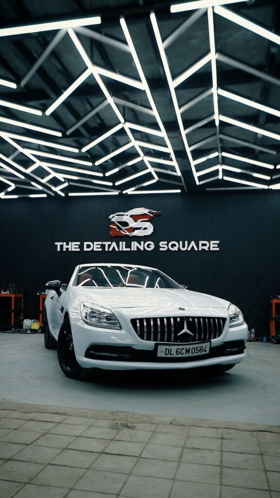 White Mercedes-Benz convertible parked under modern geometric LED ceiling lights at The Detailing Square car detailing workshop.